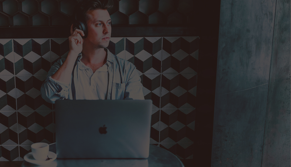 Man wearing headphones sitting with an open laptop and a cup of coffee